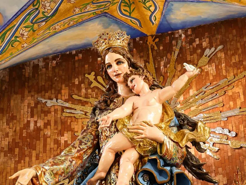 De cerca, el rostro de la Virgen con corona y el Niño en sus brazos, que levanta la paloma del Espíritu Santo.