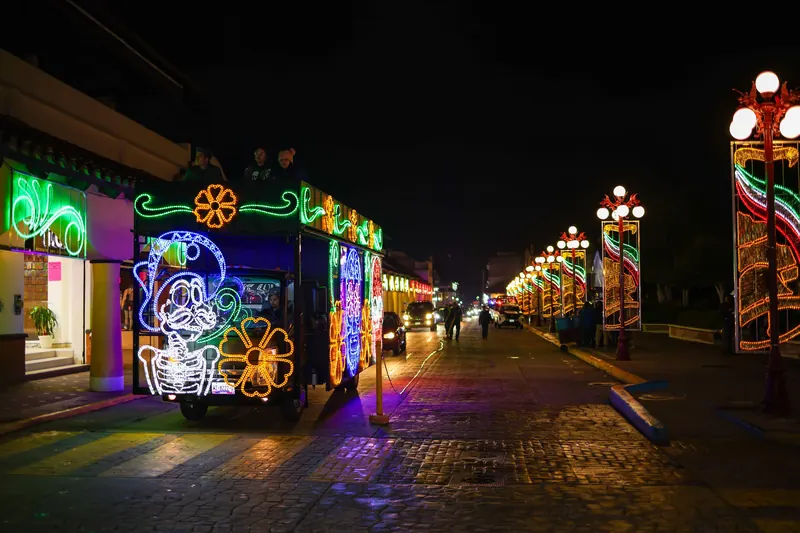 Calle del centro de noche, con faroles tricolores y un vehículo turístico cubierto de luces de colores.
