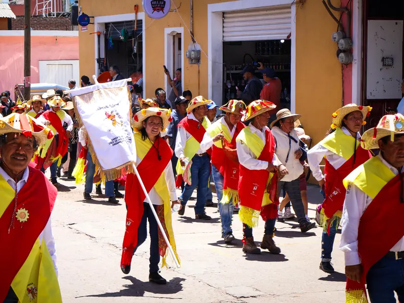 Danzantes con sombreros adornados y bandas rojas y amarillas desfilan por la calle en la fiesta de Santiago Apóstol.