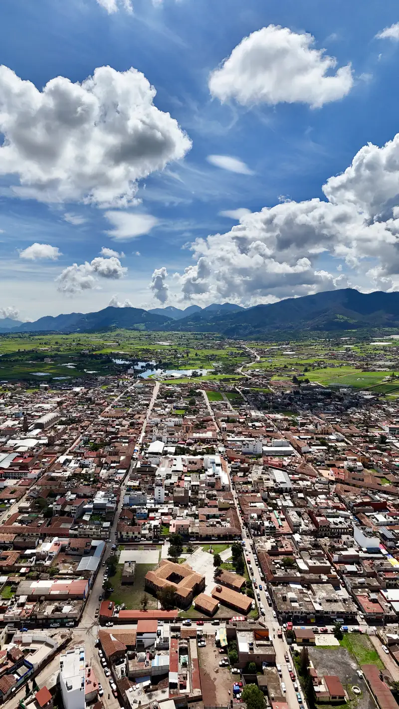 Chignahuapan from the air on a sunny day: the town, the green valley and the mountains under a blue sky with white clouds