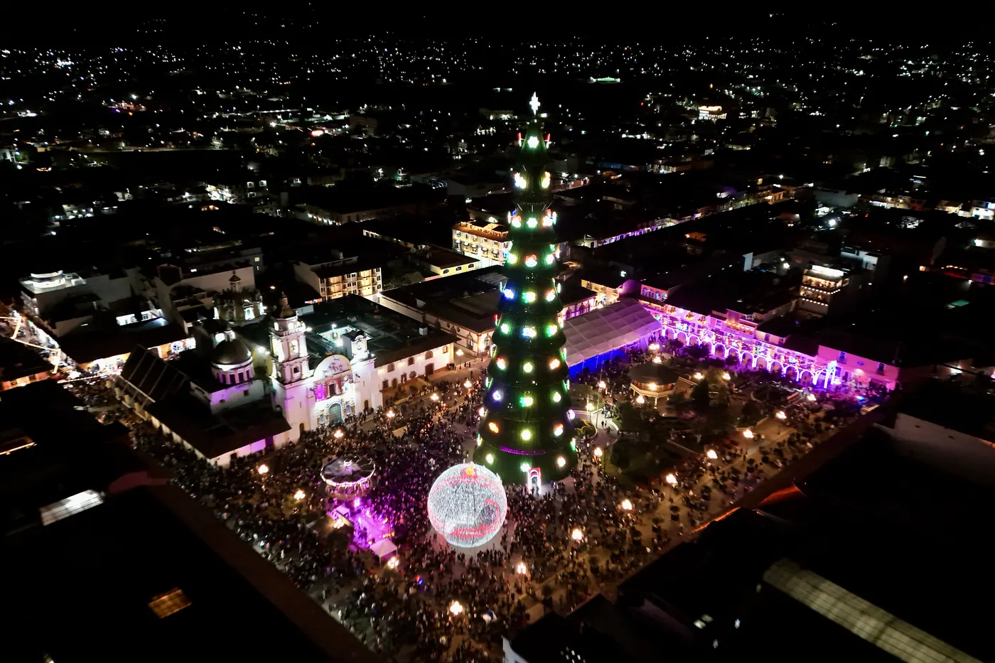 The monumental ornament and tree lit up on the plaza of Chignahuapan, seen from a drone at night, with the parish church and the plaza full of visitors