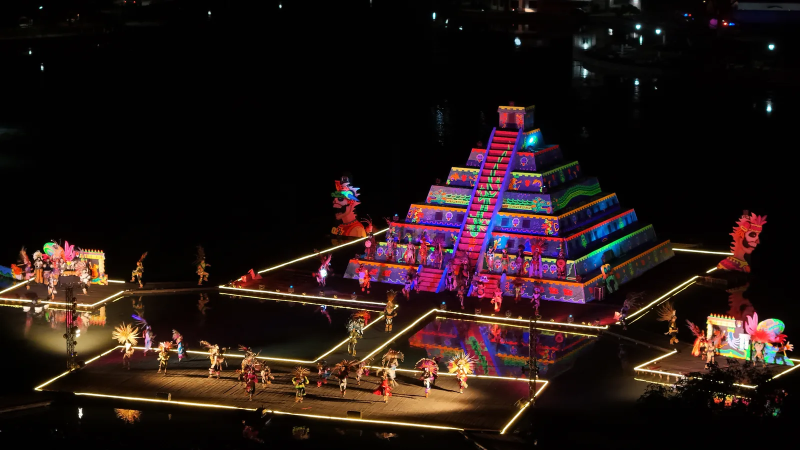 La pirámide encendida del Festival de la Luz y la Vida sobre la laguna de noche, vista desde el dron, con los danzantes en los escenarios iluminados