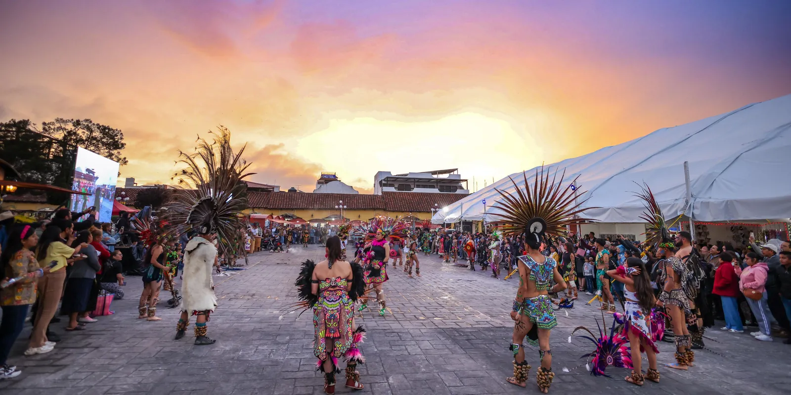 Danzantes con penachos de plumas y trajes bordados bailan en la plaza de Chignahuapan al atardecer, rodeados de visitantes