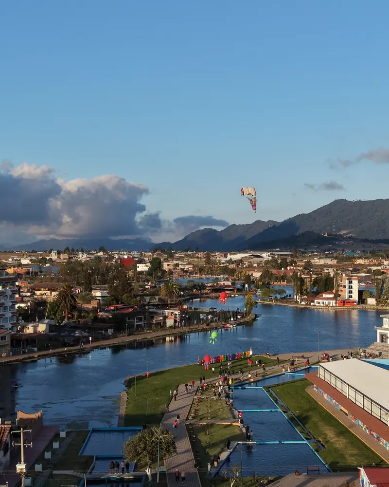 La laguna de Chignahuapan desde el aire en una tarde despejada: el agua serpentea entre el malecón y las casas del pueblo, con la sierra al fondo.