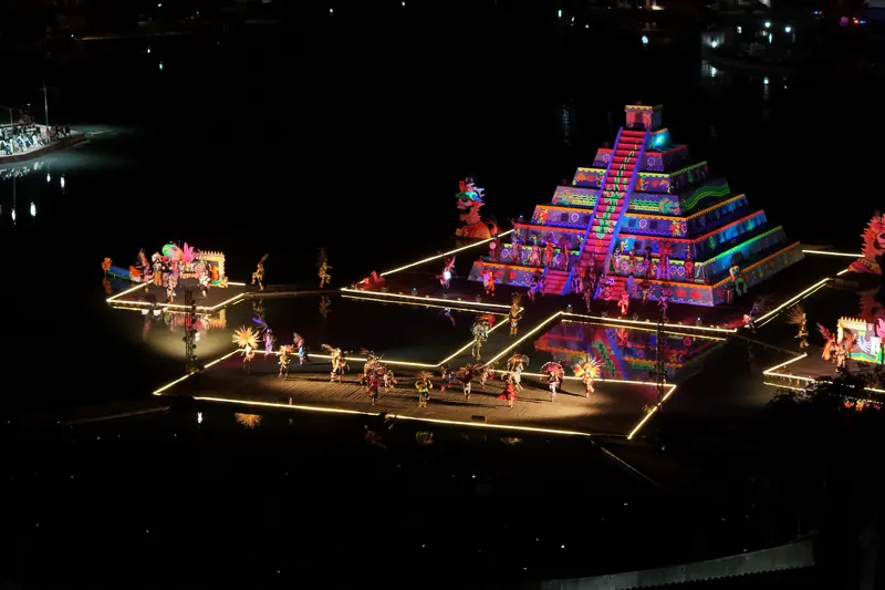 La pirámide flotante del Festival de la Luz y la Vida iluminada de noche en medio de la laguna, con los danzantes sobre los escenarios de luz.