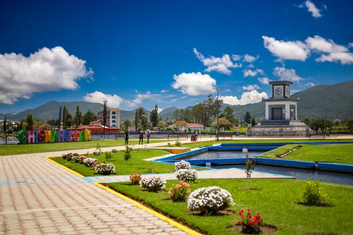 El paseo junto a la laguna en un día de cielo azul: andadores, jardines con flores, las letras de colores de Chignahuapan y el Reloj Monumental, con la sierra detrás.