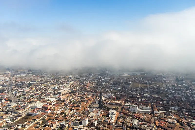 Chignahuapan from the air under a layer of mist, with the valley and the mountains behind