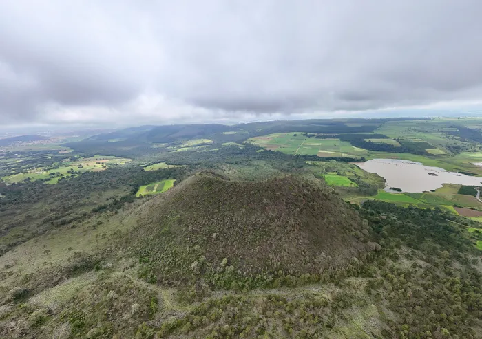 El Volcán de Chignahuapan visto desde el aire: un cono cubierto de pasto y matorral, con una laguna y campos de cultivo al fondo