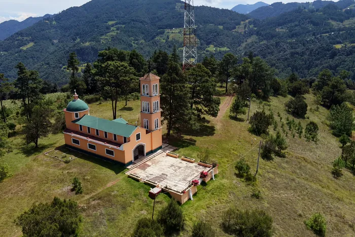 La capilla de torre rosa en lo alto del Cerrito Colorado, entre pinos y pasto, con la sierra al fondo