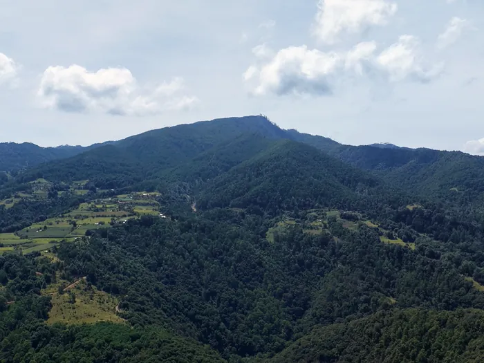 El Cerro el Quexnol cubierto de bosque bajo un cielo con nubes, con parcelas en las laderas
