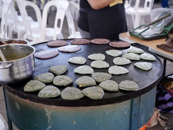 Tlacoyos de maíz azul y de maíz morado cociéndose en un comal grande, en una feria del pueblo.