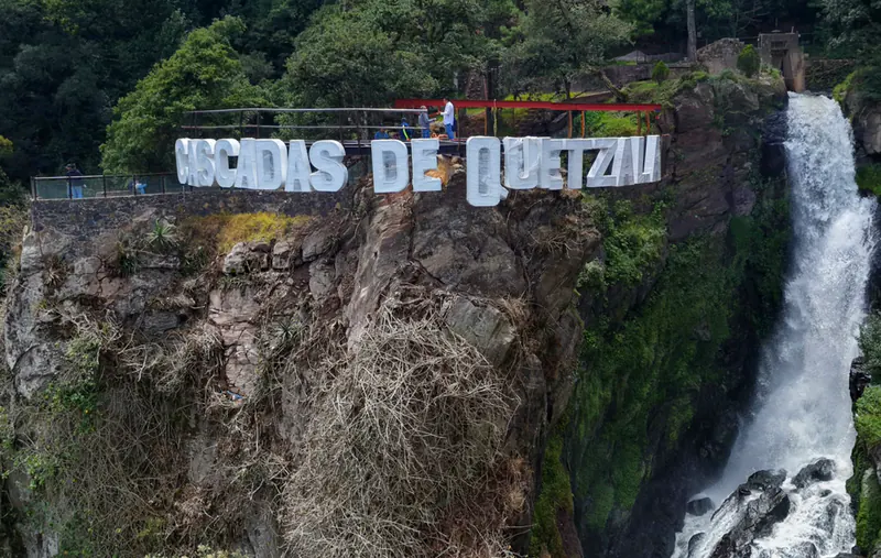 Letras monumentales de las Cascadas de Quetzalapan en lo alto del risco, junto a la caída de agua.