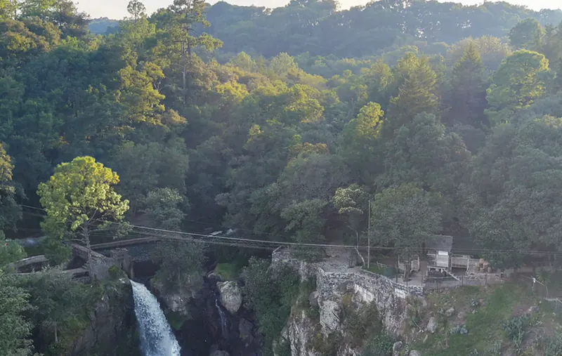 El puente colgante y el cable de la tirolesa cruzan el cañón de Quetzalapan por encima de la caída de agua, entre el bosque