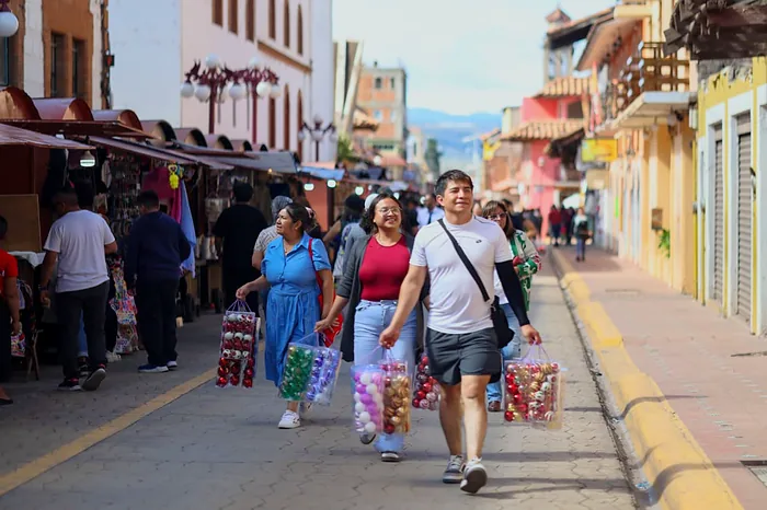 Visitantes caminan con bolsas llenas de esferas por una calle del centro de Chignahuapan