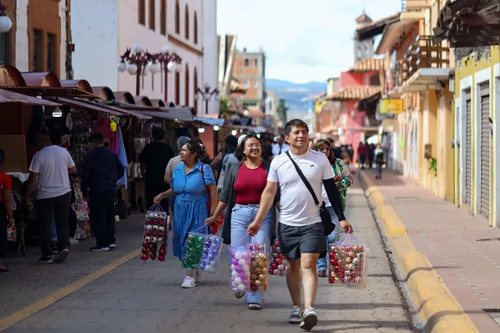 Una familia camina con sus bolsas de esferas por una calle llena de visitantes en el centro de Chignahuapan