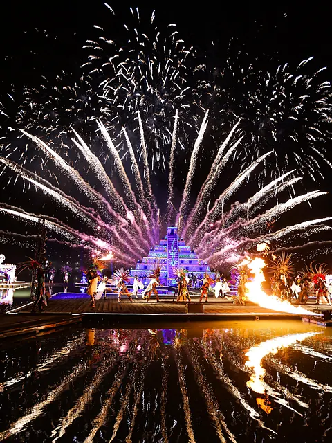 El gran final: abanicos de fuegos artificiales sobre la pirámide iluminada, reflejados en la laguna