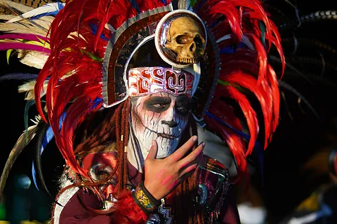 Un personaje de la puesta en escena con penacho de plumas rojas y el rostro pintado de calavera