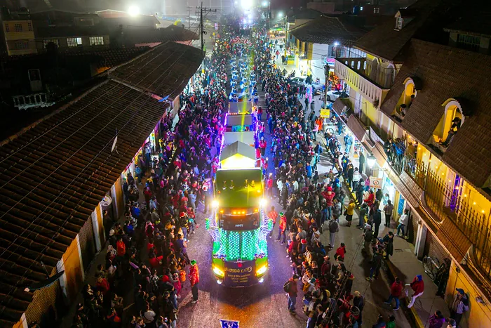 A lit-up parade float moves at night along a crowded downtown street, seen from above