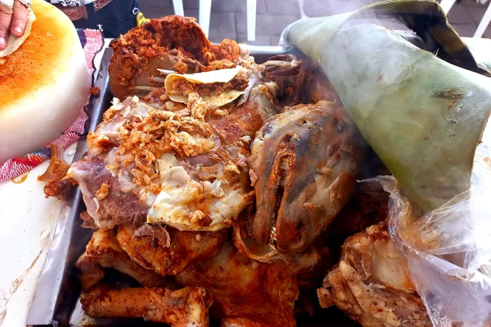 Barbacoa de hoyo recién sacada, un montón de carne dorada sobre las pencas de maguey