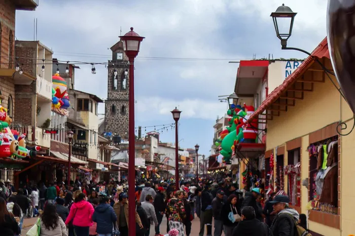 Visitantes caminando con sus compras por una calle de tiendas del centro, con la torre de la Parroquia al fondo
