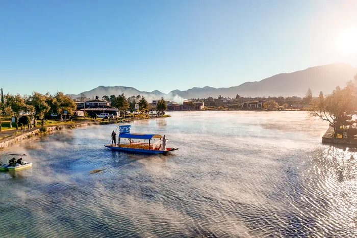 Una lancha con toldo navega por la laguna de Chignahuapan entre el vapor del agua, con la sierra al fondo