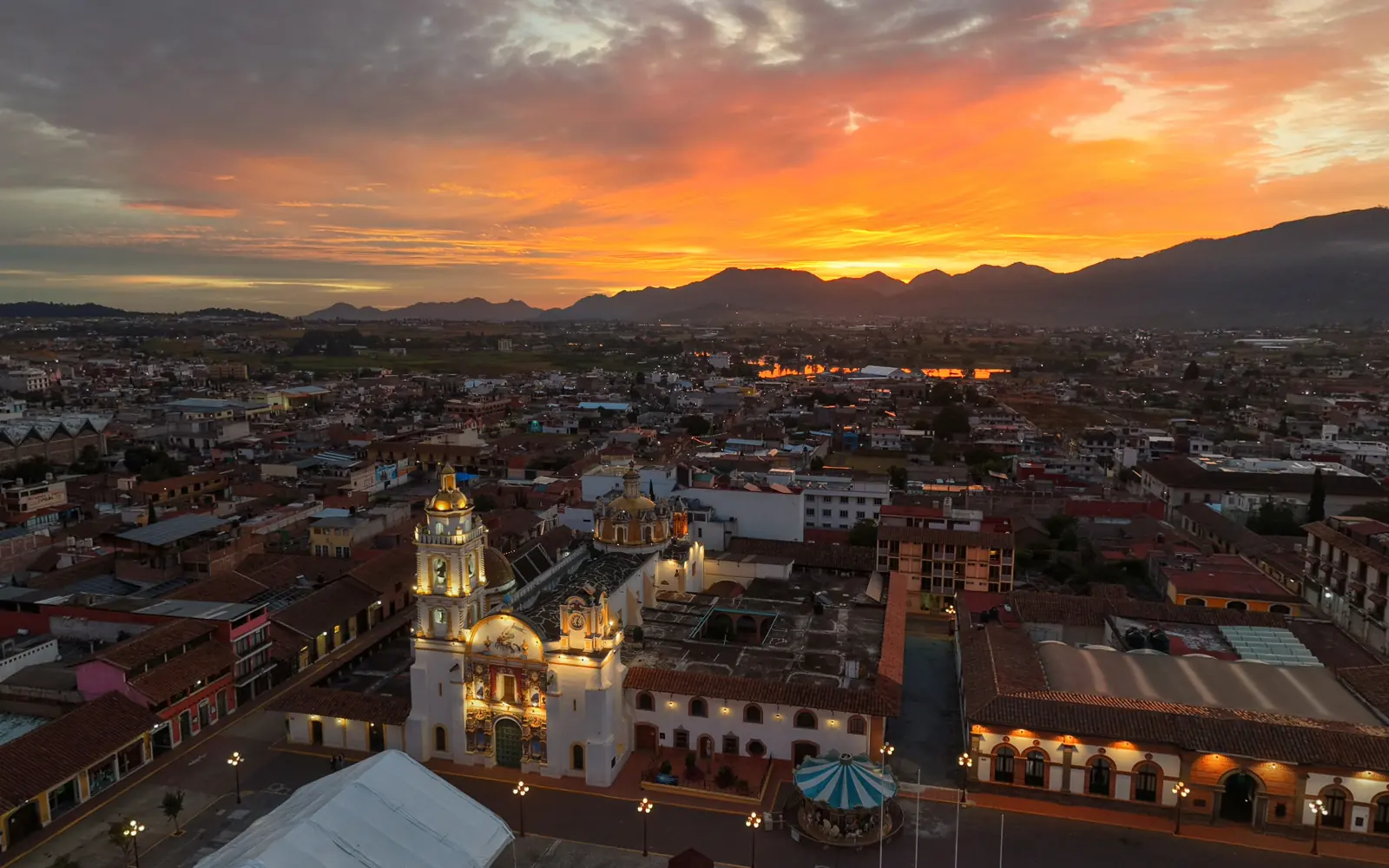 Downtown Chignahuapan at sunrise, with the parish church lit up and a glowing sky over the mountains