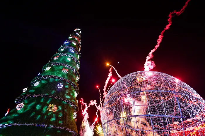 The monumental tree and ornament lit up at night, with fireworks rising next to the ornament of lights