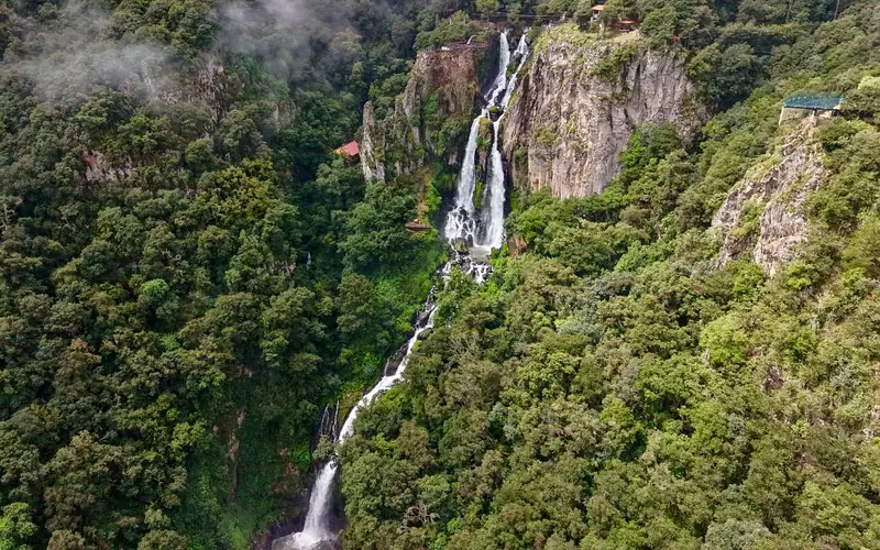 The Quetzalapan waterfalls seen from the side: the water drops down the rock face through the mist and the mountain forest