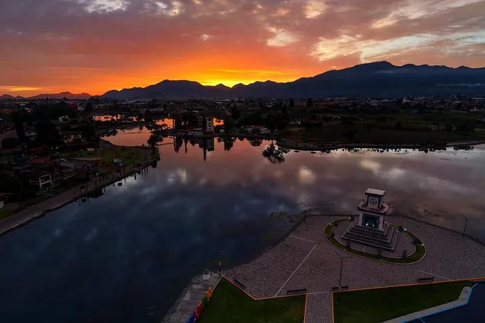 La laguna de Chignahuapan al amanecer vista desde el aire, con el cielo naranja reflejado en el agua quieta y la sierra al fondo
