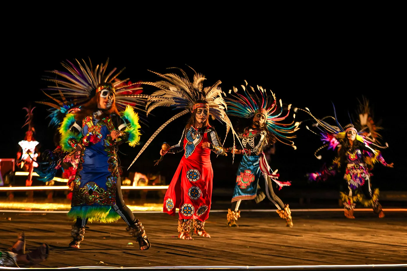 Danzantes con penachos de plumas y trajes de colores bailan de noche en el escenario del Festival de la Luz y la Vida