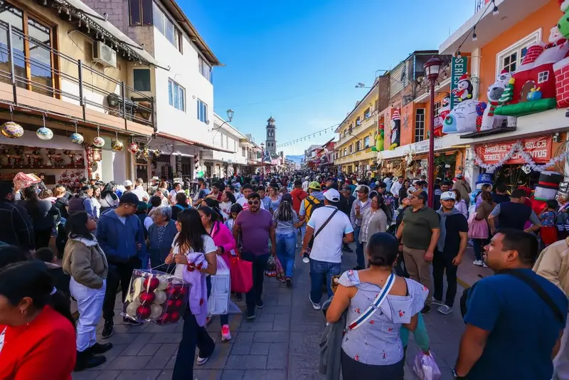A downtown Chignahuapan street full of visitors among ornament and Christmas decoration shops, with the parish church tower in the background