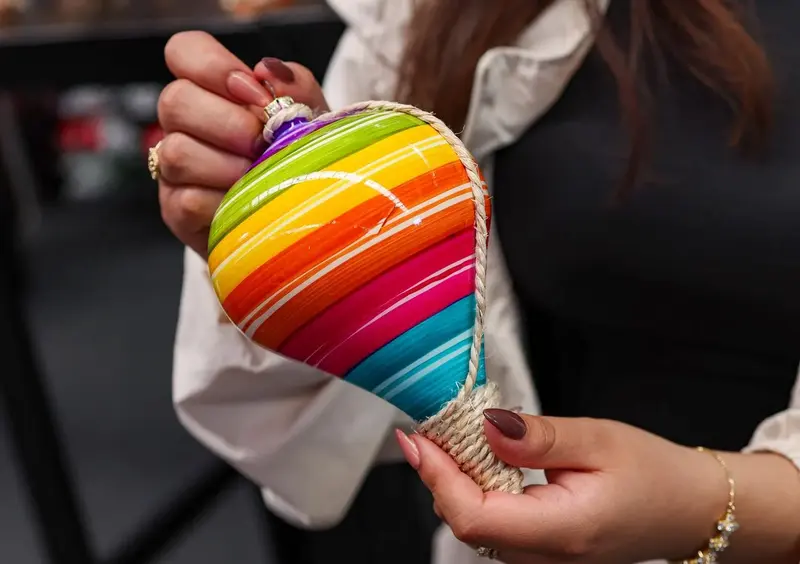 Hands hold a finished ornament striped in every color of the rainbow