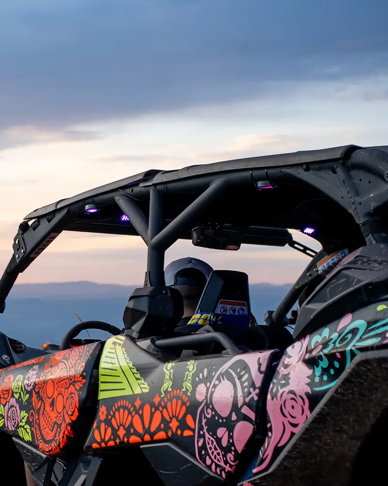 Un vehículo todoterreno decorado con calaveras de colores en un mirador de la sierra al atardecer, con el valle y los volcanes al fondo