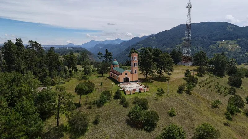 La capilla de El Calvario en lo alto del Cerrito Colorado, entre pinos, con la sierra y las montañas detrás.