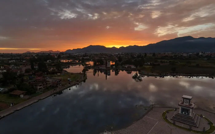 Amanecer naranja sobre la sierra reflejado en la laguna de Chignahuapan, con el malecón en primer plano.