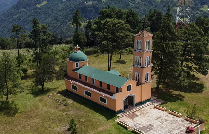 La iglesia del Calvario, en el Cerrito Colorado, vista desde el aire: muros color durazno, techo y cúpula verdes y campanario, entre pinos y pasto.