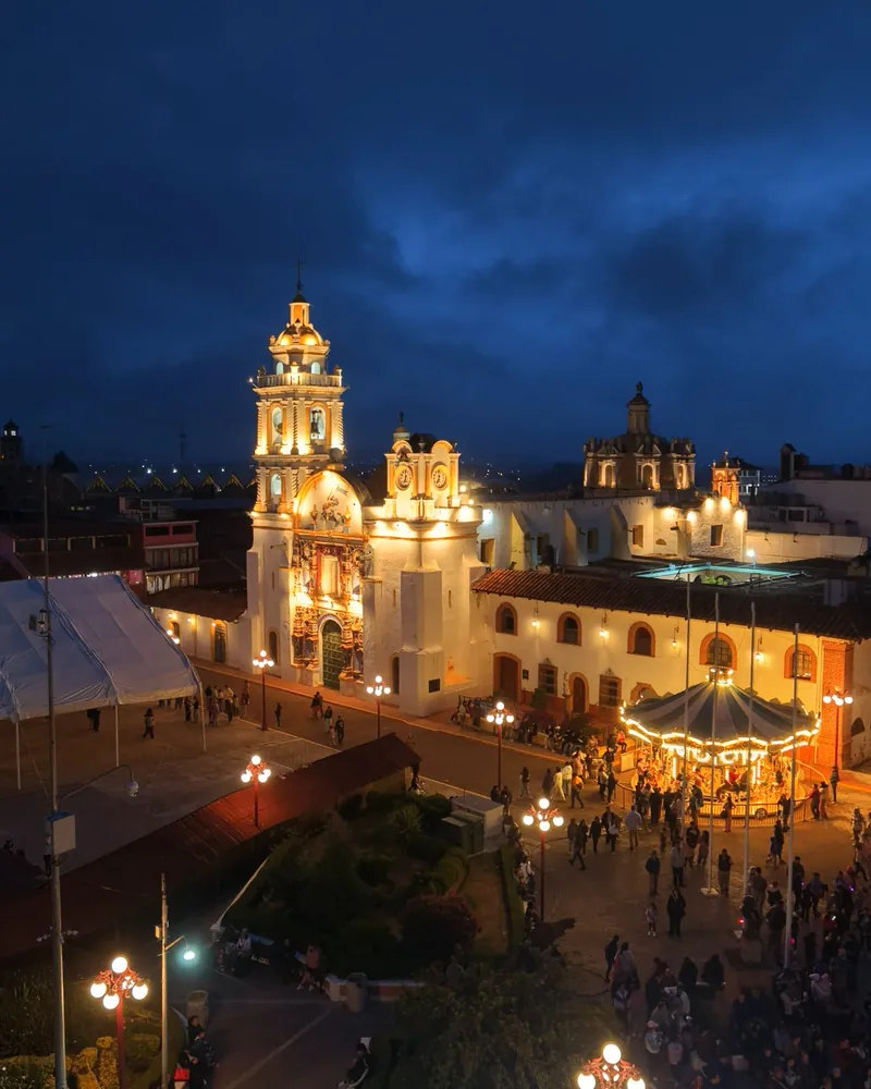 La Parroquia de Santiago Apóstol iluminada a la hora azul, con la plaza de Chignahuapan llena de gente.