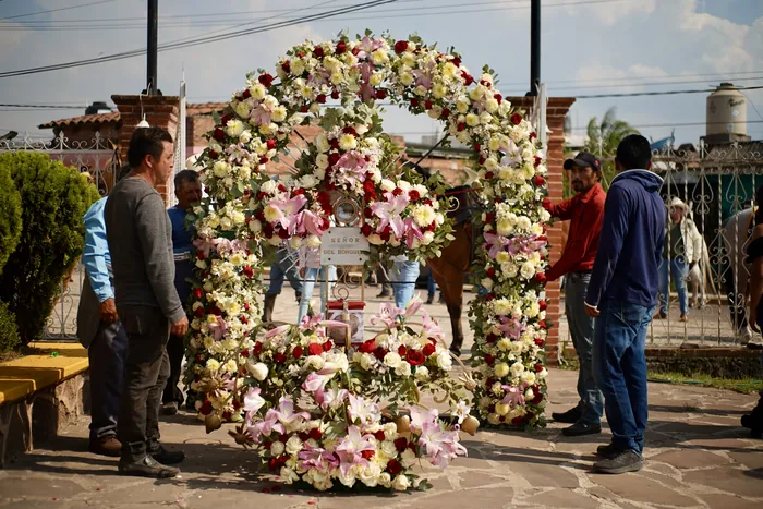 Un gran arco de flores blancas, rosas y rojas en el atrio, con fieles a su alrededor.