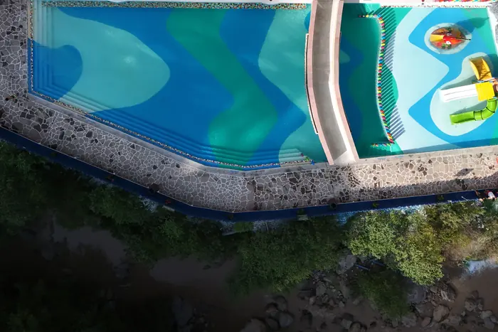 Two thermal water pools seen from above, their bottoms painted in blue and green waves, on the edge of the ravine.