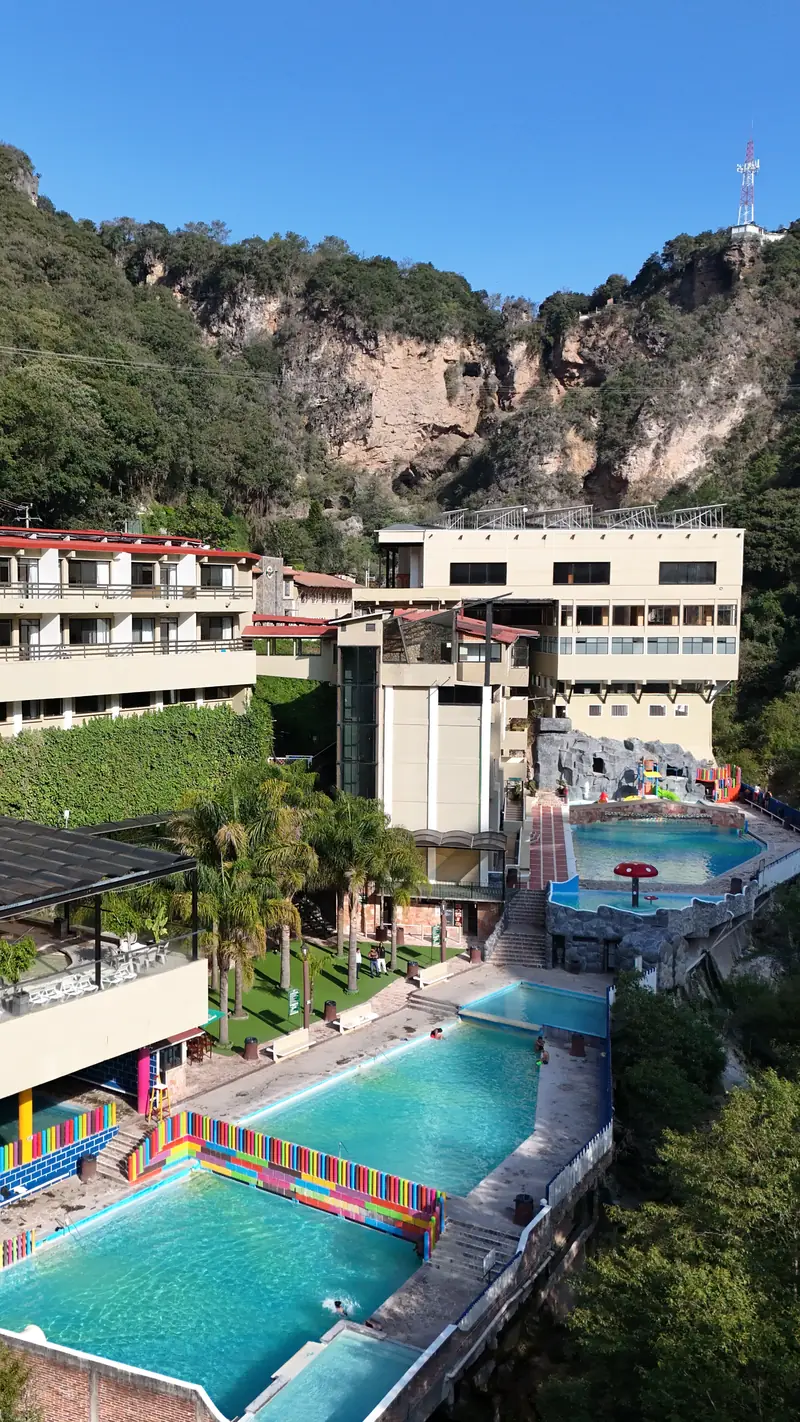 The Chignahuapan hot springs ravine from the air: turquoise pools at the foot of the hill, surrounded by forest and rock walls.